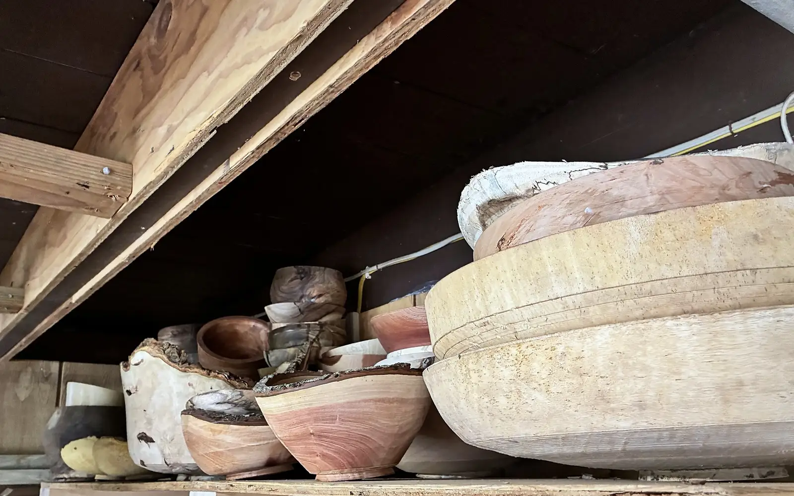 Bowls on a high shelf in Kaleb’s shop, in pale, pink and spalted woods, some with the bark left on the rim