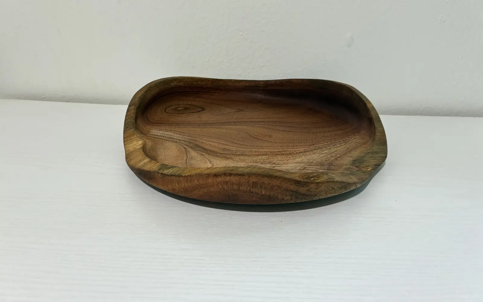 Kaleb’s free-form platter on a white shelf, its grain circling a knot near one edge