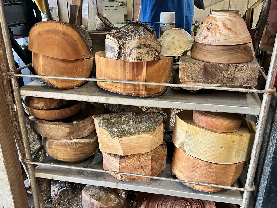 Kaleb’s rack of wood in the shop: rounds cut from the log, rough-turned bowls and blanks with the bark still on