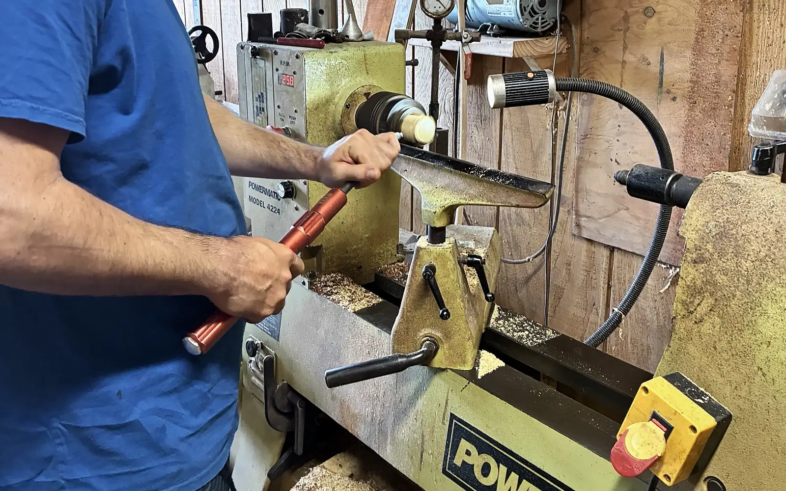 Kaleb turning at the lathe in a face shield, the tool steady on the rest and shavings on the bed